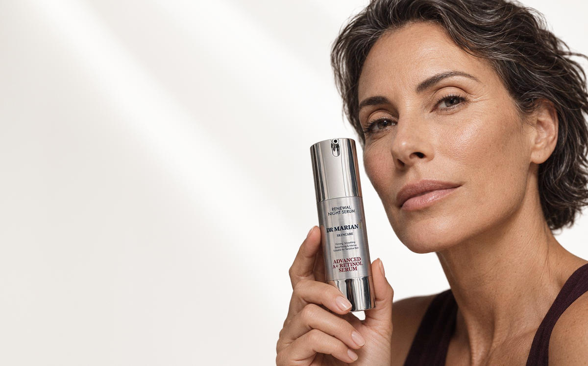 A woman holding a silver Dr. Marian Advanced Retinol serum bottle against a clean, light off-white background.